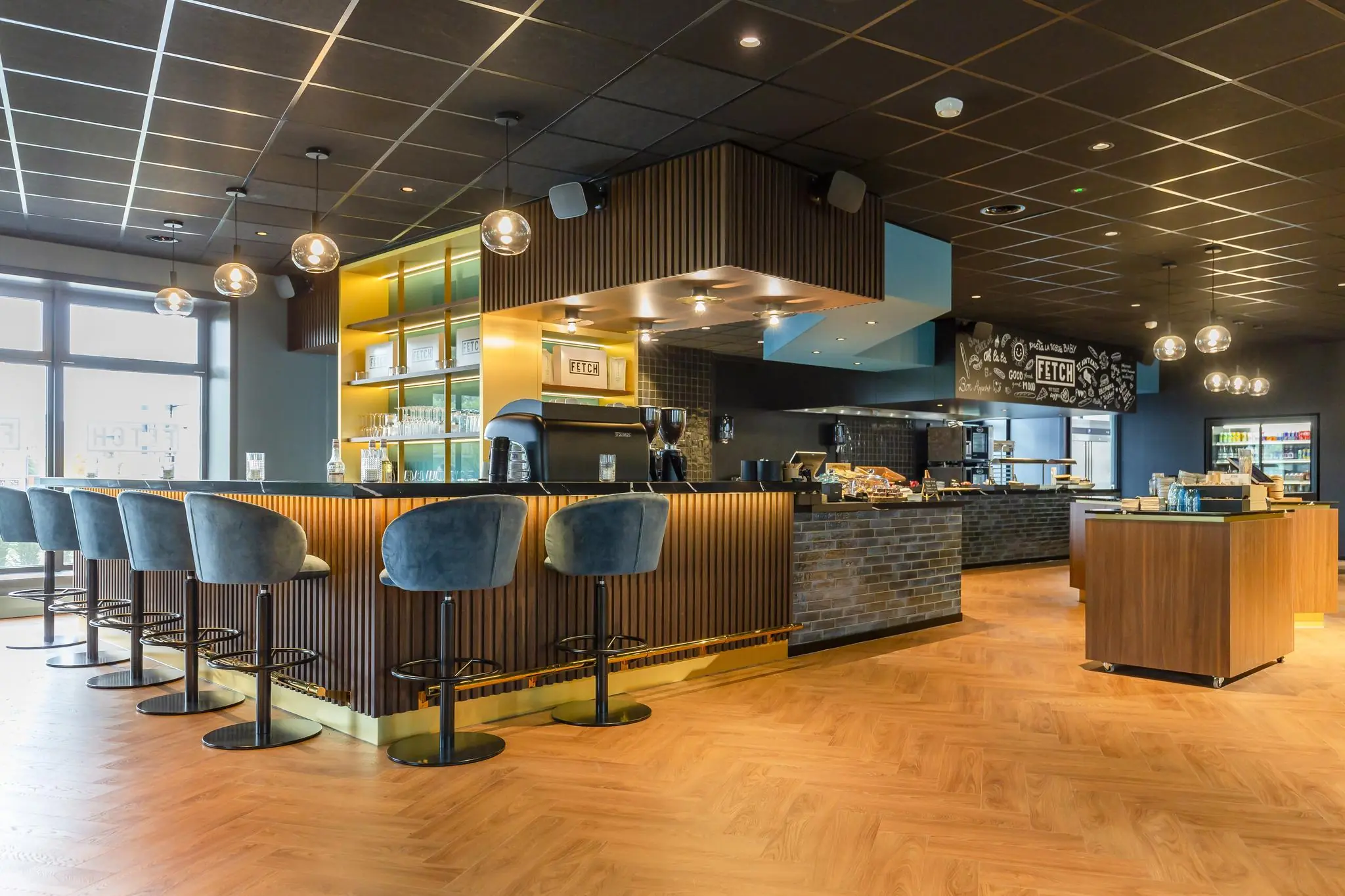 Modern ingerichte koffie- en lunchbar aan de George Hintzenweg met een centraal eiland, barkrukken en warme houten accenten.